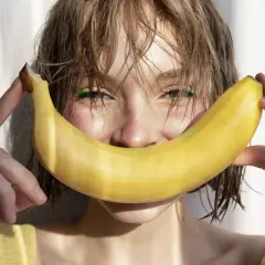 Uśmiechnięta dziewczyna z bananem, który przypomina uśmiech. Banan jest bogaty w potas, a chlorek potasu jest jego ważnym związkiem.
