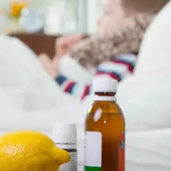 Cytryna, syrop i leki na przeziębienie dla dziecka leżą obok łóżka, gdzie odpoczywa chory maluch.