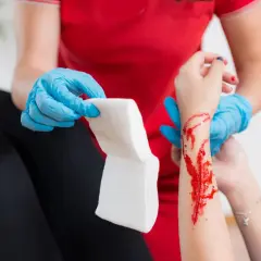 Opatrunek na ręce z raną, która może być objawem hemofilii. Osoba w niebieskich rękawiczkach przygotowuje gazę.
