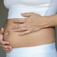 Kobieta trzyma się za brzuch, odczuwając dyskomfort związany z wzdęciami.