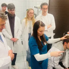 Grupa lekarzy i studentów w białych fartuchach obserwuje badanie pacjenta na nowoczesnym sprzęcie medycznym.