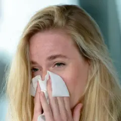 Kobieta z blond włosami chusteczką wyciera nos. Może potrzebuje loratadyna galena na alergię.