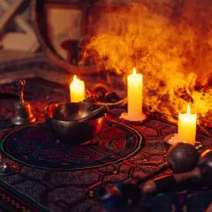 Obrzędowa atmosfera z palącymi się świecami, misą, dzwonkiem i marakasami, sugerująca ceremonię z użyciem ayahuasca.