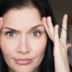 Kobieta zmarszczkami na czole, dotykająca skroni. Jej twarz, choć zadbana, zdaje się być odzwierciedleniem efektu "ozempic face".