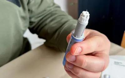 Dłoń trzymająca wstrzykiwacz z igłą. Osoba przygotowuje się do podania leku, być może zastanawiając się nad potencjalnymi mounjaro skutki uboczne.