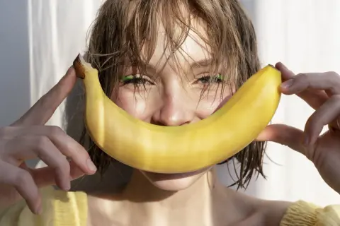 Uśmiechnięta dziewczyna z bananem, który przypomina uśmiech. Banan jest bogaty w potas, a chlorek potasu jest jego ważnym związkiem.