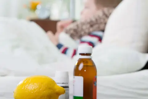 Cytryna, syrop i leki na przeziębienie dla dziecka leżą obok łóżka, gdzie odpoczywa chory maluch.
