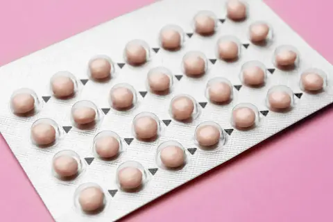Blister opakowania tabletek antykoncepcyjnych na różowym tle.