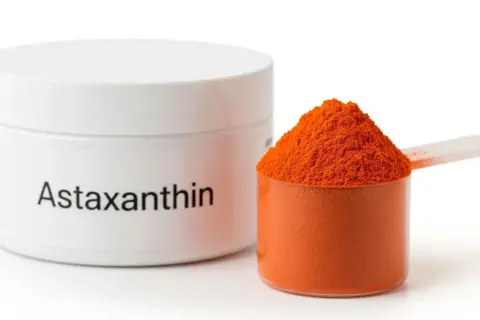Słoiczek z napisem "Astaxanthin" obok miarki wypełnionej pomarańczowym proszkiem. Ten silny antyoksydant, astaksantyna, jest gotowy do użycia.