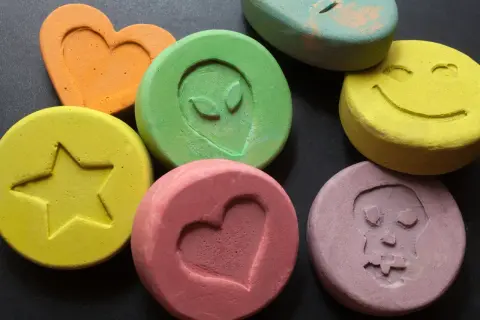Kolorowe tabletki z symbolami: serce, uśmiech, czaszka, gwiazda, kosmita. To mogą być tabletki MDMA.