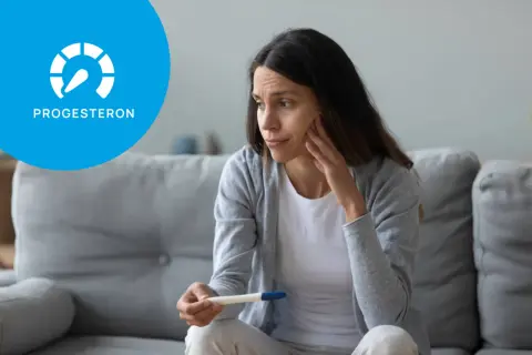 Zmartwiona kobieta trzyma test ciążowy. Ikona z napisem "PROGESTERON" sugeruje, że może to być związane z niskim progesteronem objawy.