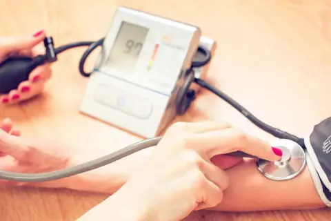 Dwie osoby mierzą ciśnienie. Jedna ręka trzyma pompkę, druga stetoskop. Na ekranie ciśnieniomierza widnieje wynik 97. To ważny pomiar dla zdrowia, jak ten z hygrotonem.
