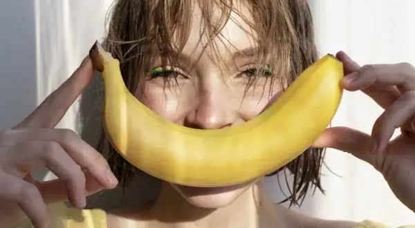 Uśmiechnięta dziewczyna z bananem, który przypomina uśmiech. Banan jest bogaty w potas, a chlorek potasu jest jego ważnym związkiem.