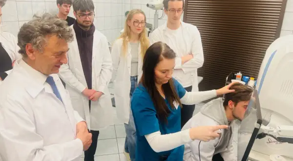 Grupa lekarzy i studentów w białych fartuchach obserwuje badanie pacjenta na nowoczesnym sprzęcie medycznym.