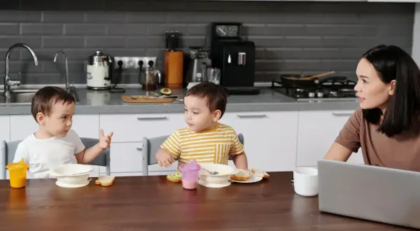 Mama rozmawia z dziećmi przy stole, gdy dziecko zaczyna mówić, gestykulując.