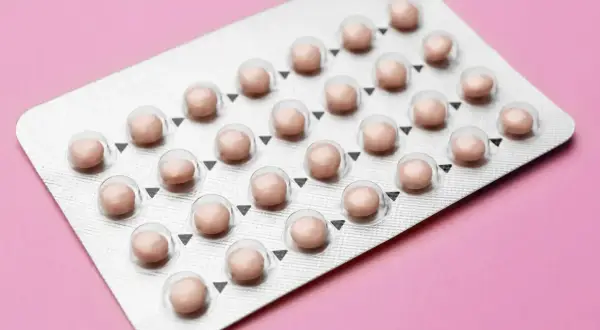 Blister opakowania tabletek antykoncepcyjnych na różowym tle.