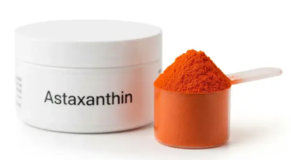 Słoiczek z napisem "Astaxanthin" obok miarki wypełnionej pomarańczowym proszkiem. Ten silny antyoksydant, astaksantyna, jest gotowy do użycia.