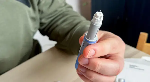 Dłoń trzymająca wstrzykiwacz z igłą. Osoba przygotowuje się do podania leku, być może zastanawiając się nad potencjalnymi mounjaro skutki uboczne.