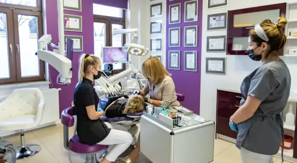 Gabinet stomatologiczny z trzema osobami w maskach, w tym dentystką przy pacjencie.