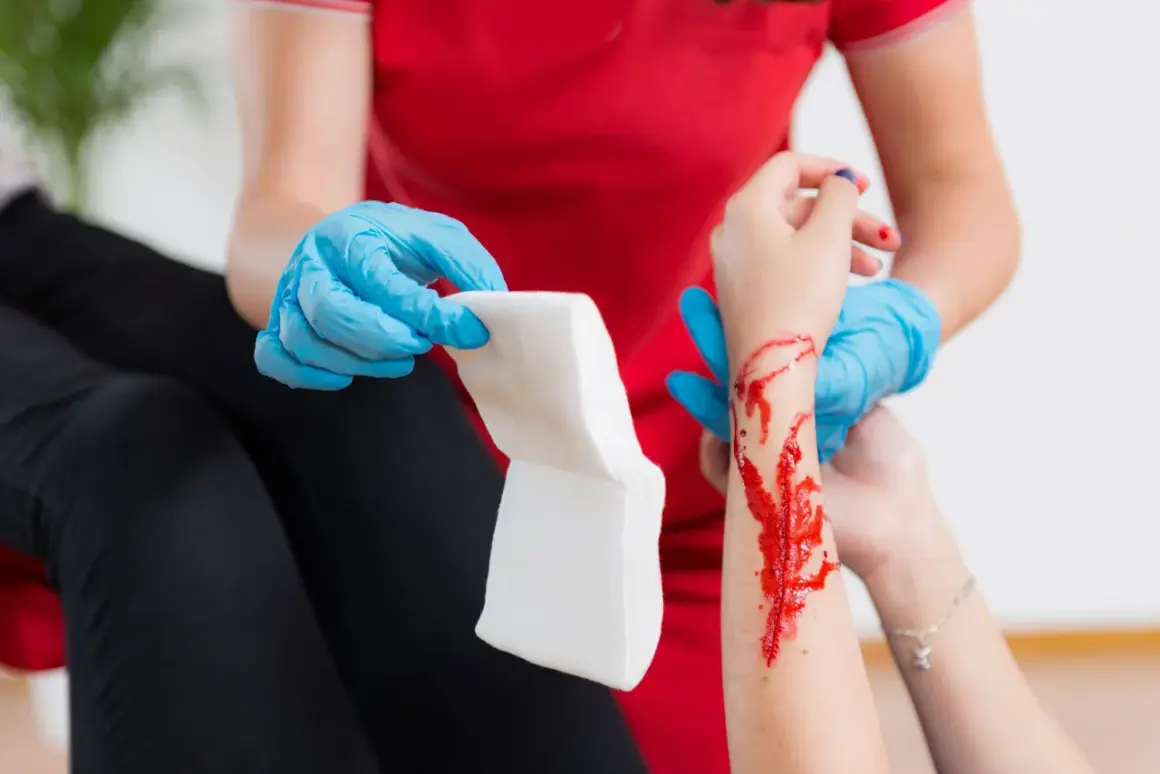 Opatrunek na ręce z raną, która może być objawem hemofilii. Osoba w niebieskich rękawiczkach przygotowuje gazę.