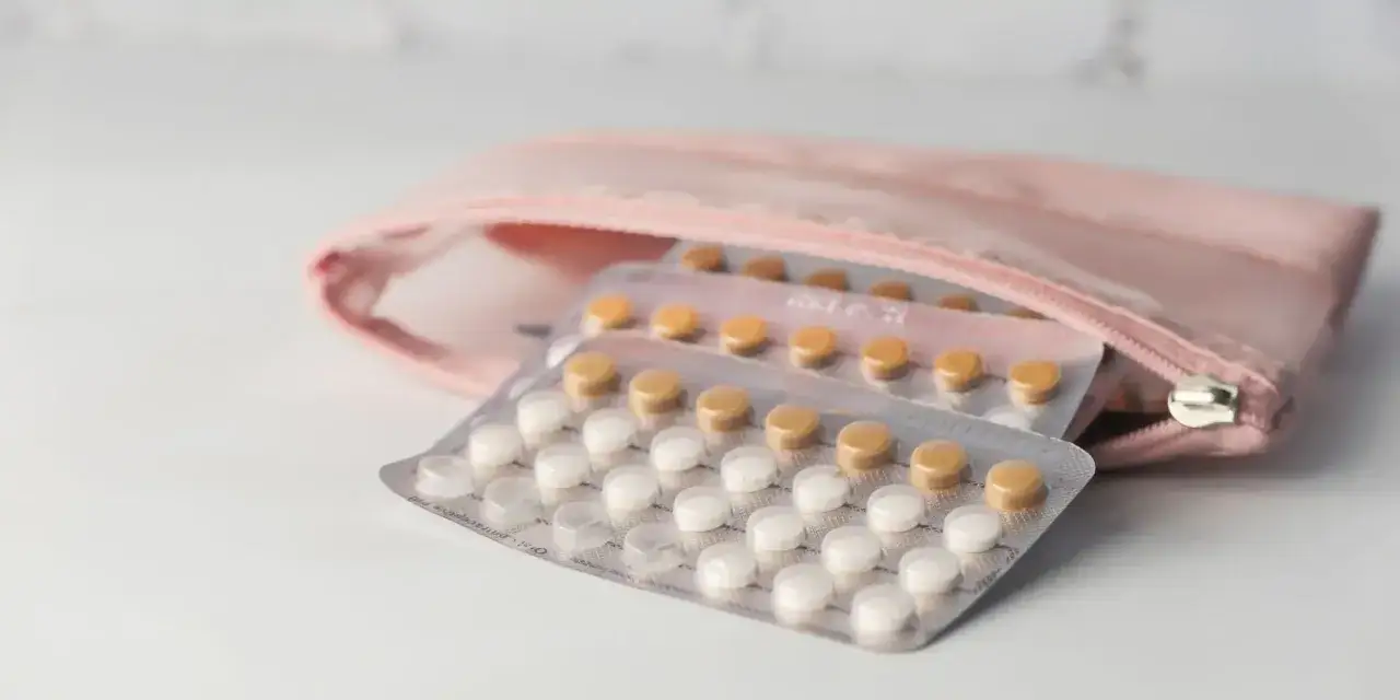Pigułki antykoncepcyjne w blistrach, gotowe do codziennego stosowania, schowane w różowej kosmetyczce.