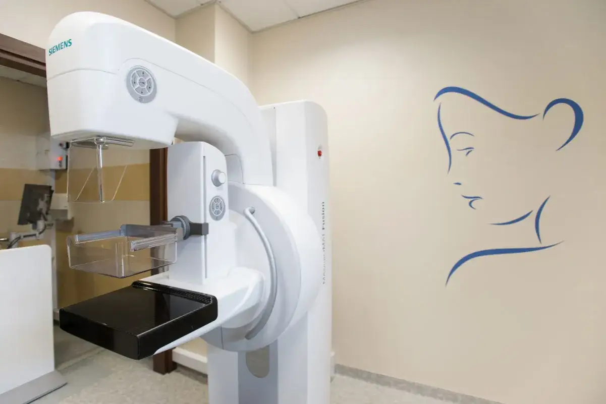 Nowoczesny aparat do mammografii Siemens, obok stylizowany rysunek twarzy kobiety. Dbanie o zdrowie zaczyna się od profilaktyki.