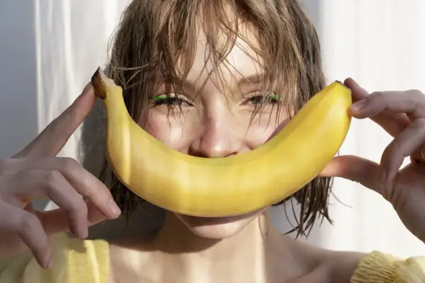 Uśmiechnięta dziewczyna z bananem, który przypomina uśmiech. Banan jest bogaty w potas, a chlorek potasu jest jego ważnym związkiem.