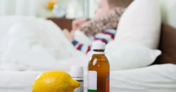 Cytryna, syrop i leki na przeziębienie dla dziecka leżą obok łóżka, gdzie odpoczywa chory maluch.