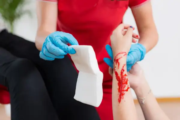 Opatrunek na ręce z raną, która może być objawem hemofilii. Osoba w niebieskich rękawiczkach przygotowuje gazę.