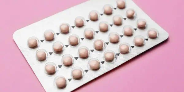 Blister opakowania tabletek antykoncepcyjnych na różowym tle.