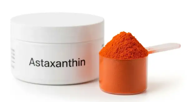 Słoiczek z napisem "Astaxanthin" obok miarki wypełnionej pomarańczowym proszkiem. Ten silny antyoksydant, astaksantyna, jest gotowy do użycia.